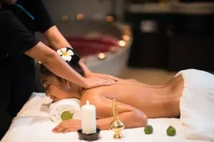 Woman receiving a relaxing Swedish massage in a spa setting, lying face down on a massage table with candles, flower decor, and warm ambient lighting.